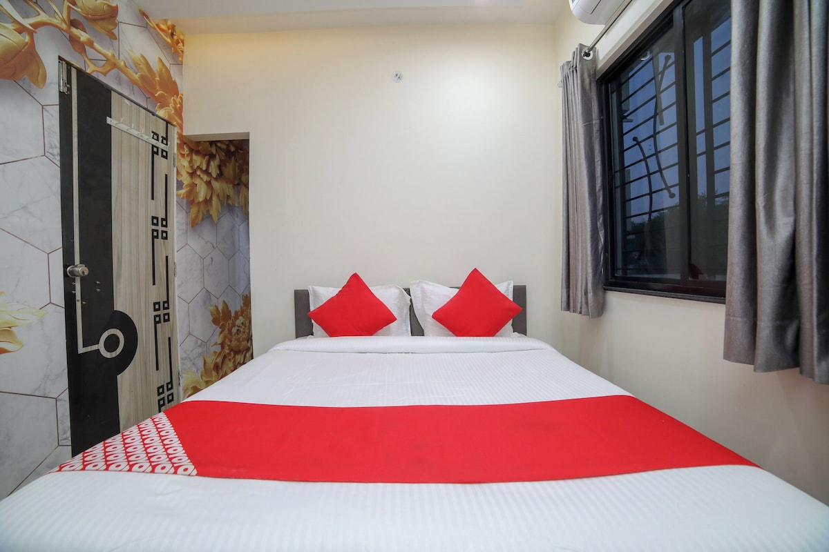 A hotel room with a bed, a window with curtains, a wall clock, and a door with a decorative design.