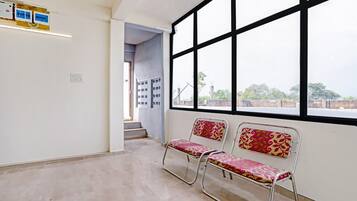 A waiting area with two metal chairs, a window with black frames, and a wall-mounted electrical panel.