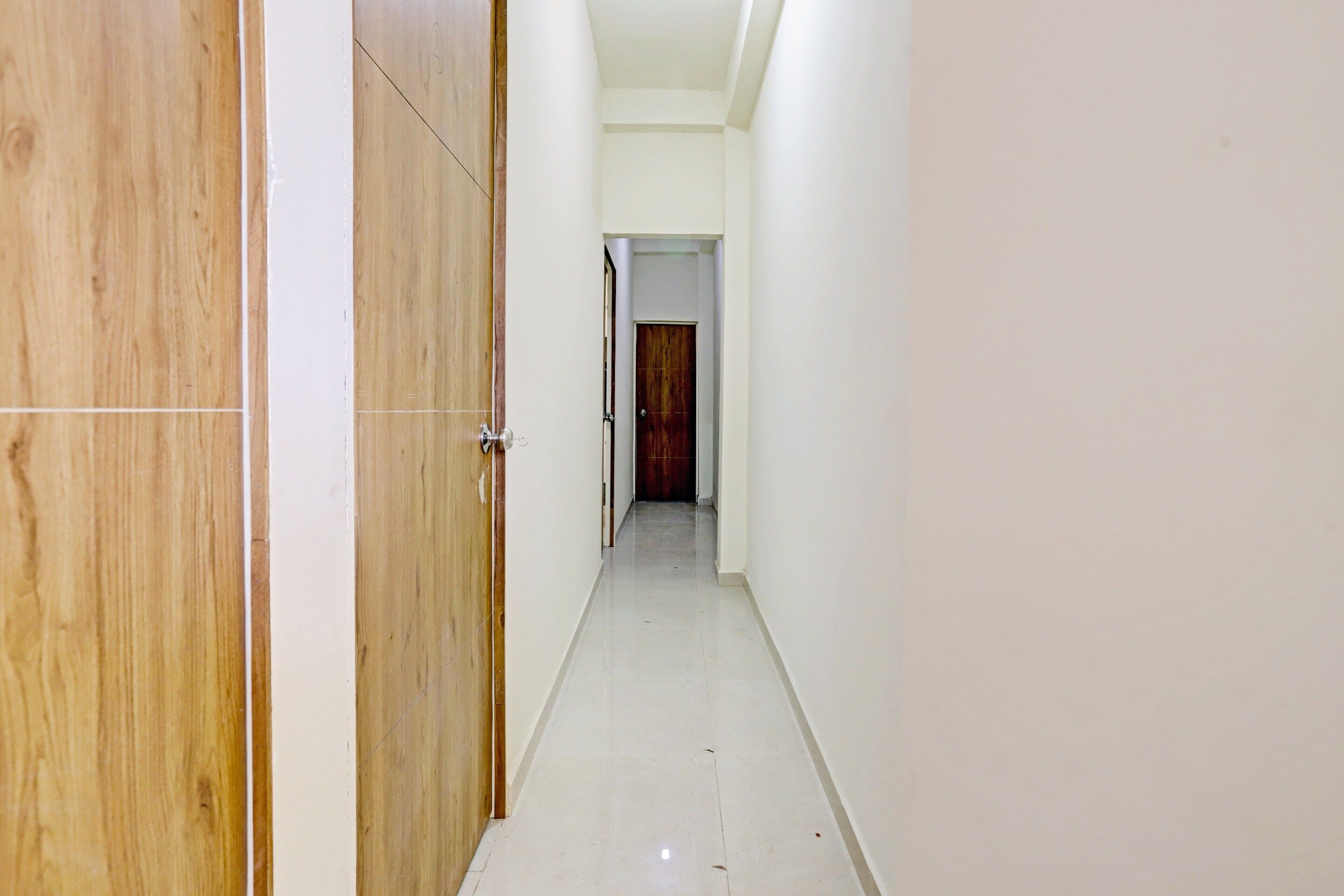 A narrow hallway with wooden doors on one side and white walls on the other.