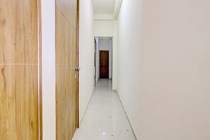 Un pasillo estrecho con puertas de madera a un lado y paredes blancas al otro.