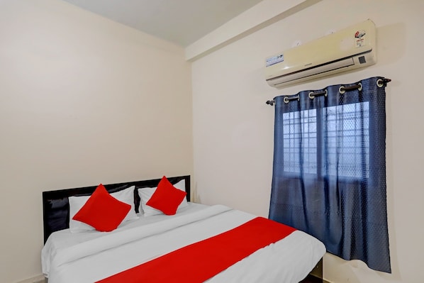 A hotel room with a bed, a red and white bedspread, a blue curtain, and an air conditioning unit. - Hotel O Casino (Kamptee)
