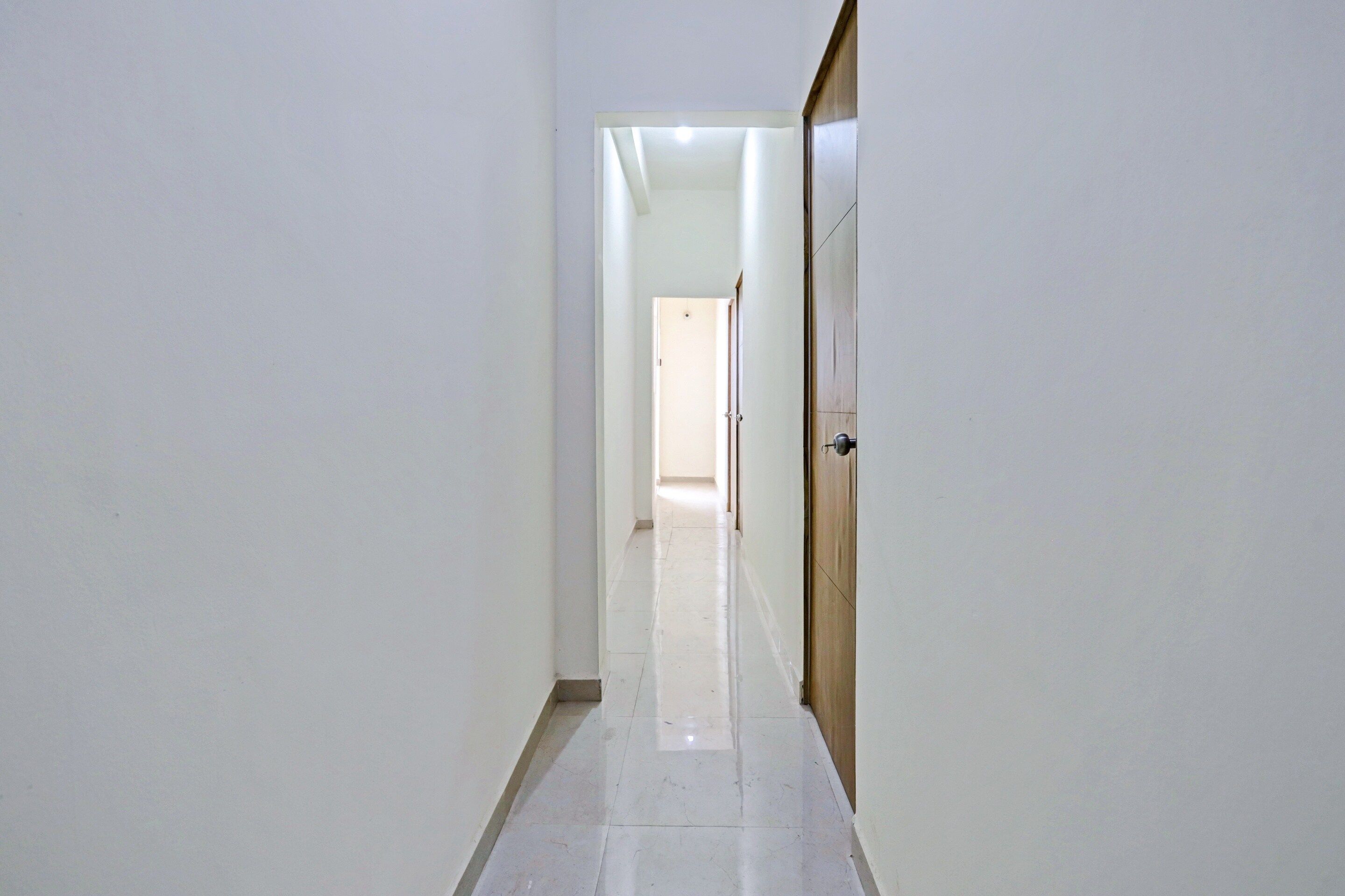A corridor with a wooden door on the right, leading to a room with a tiled floor.
