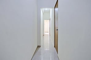 A corridor with a wooden door on the right, leading to a room with a tiled floor. - Hotel O Casino (Kamptee)
