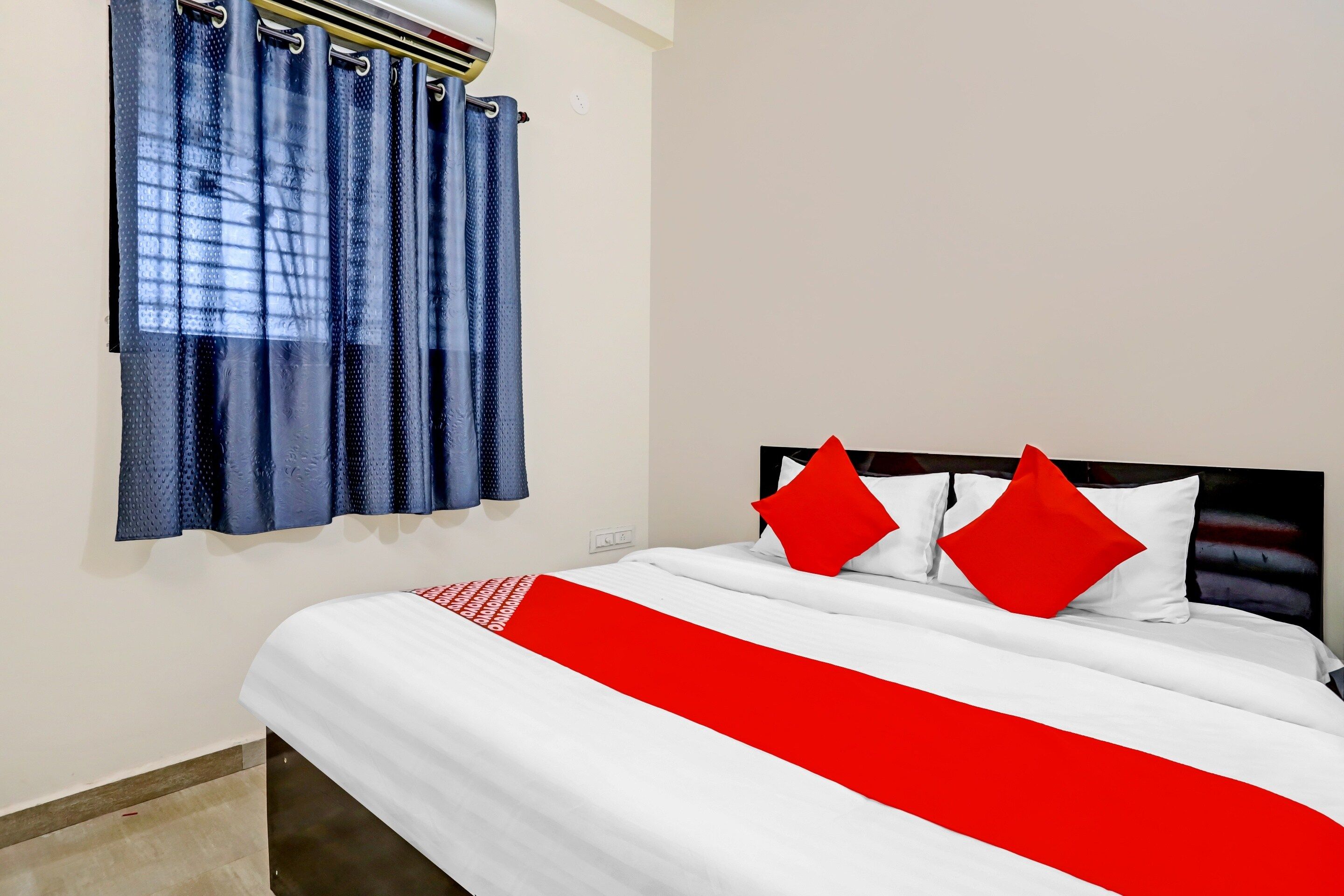 A hotel room with a bed, a window with blue curtains, and a wall-mounted air conditioning unit.