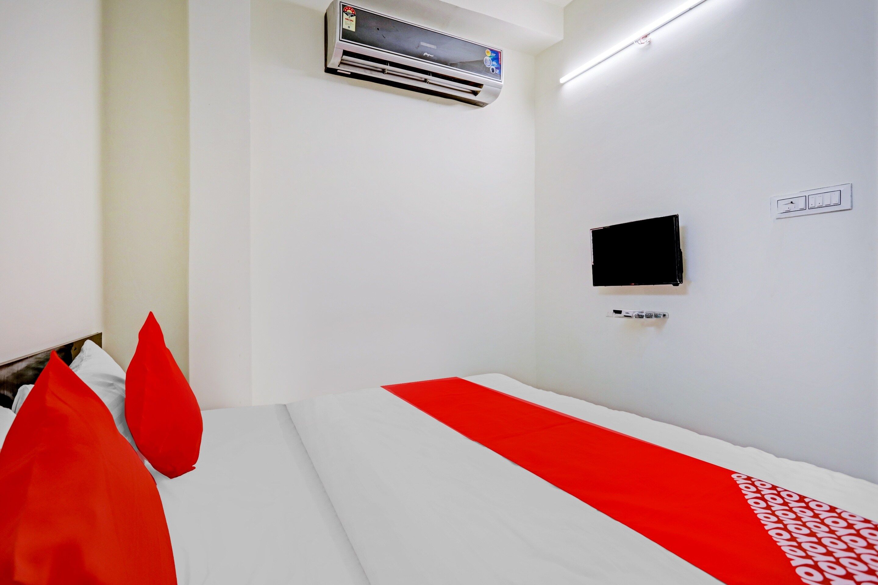 Habitació d'hotel amb un llit, un televisor de pantalla plana penjat a la paret, un aparell d'aire condicionat sobre el llit i una presa de corrent a la paret.