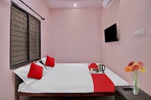 A hotel room with a bed, a TV, a window with blinds, and a vase with flowers. - Hotel O R K Guest House (Nagpur)