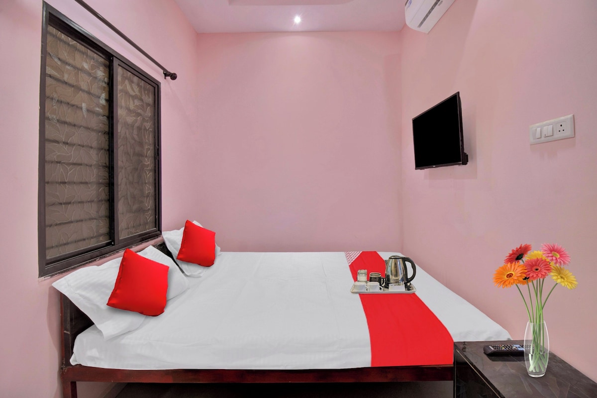 A hotel room with a bed, a TV, a bedside table, and a vase with flowers.