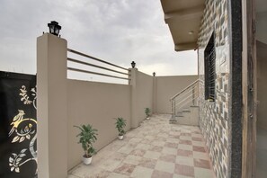 Una terraza en la azotea con piso a cuadros, plantas en macetas, baranda metálica y pared con diseño geométrico.