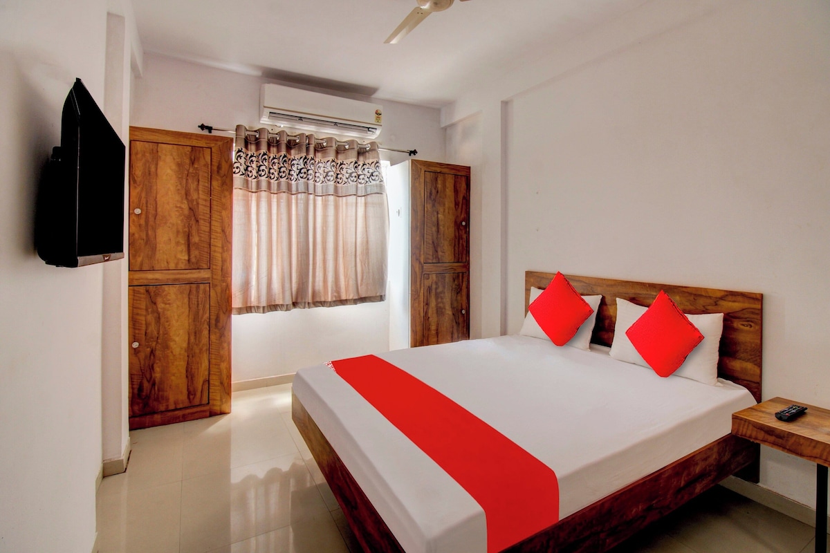 A hotel room with a bed, a TV, a wardrobe, and an air conditioning unit.