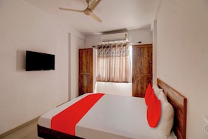 A bedroom with a bed, a ceiling fan, an air conditioning unit, a television mounted on the wall, and wooden wardrobes. - Hotel O The Golden Key (Nagpur)