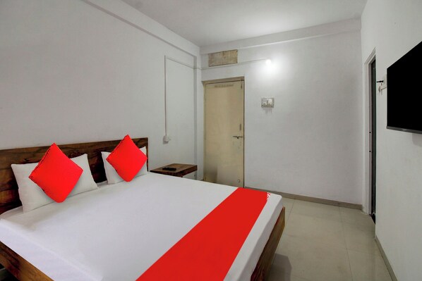 A hotel room with a bed, a bedside table, a TV mounted on the wall, and a door. - Hotel O The Golden Key (Nagpur)