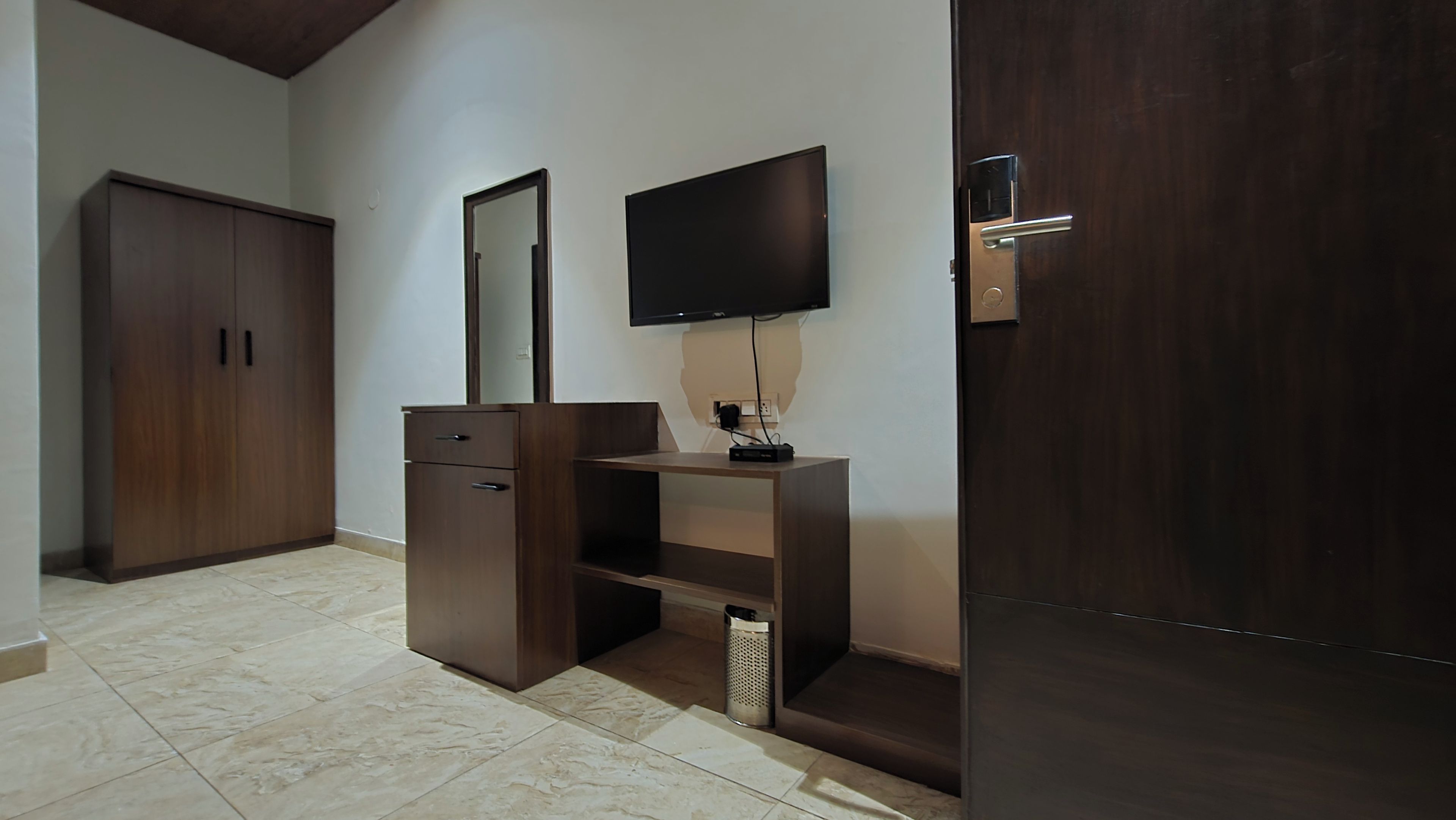 A room with a wooden wardrobe, a TV mounted on the wall, and a door with a modern handle.