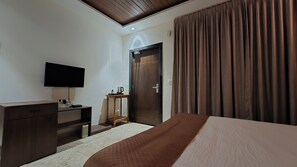 A hotel room with a bed, a TV, a wooden dresser, a coffee table, and a door. - The Imperial Beach Resort (Shrivardhan)