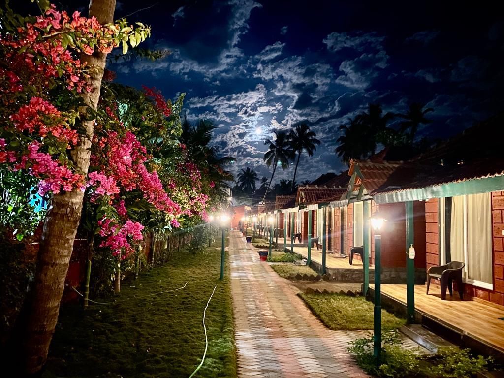 A pathway leading to a row of buildings with outdoor seating areas, surrounded by lush greenery and flowering plants.