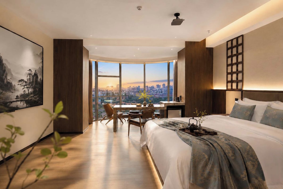 Een moderne hotelkamer met een groot bed, een bureau en uitzicht op een stadsgezicht.