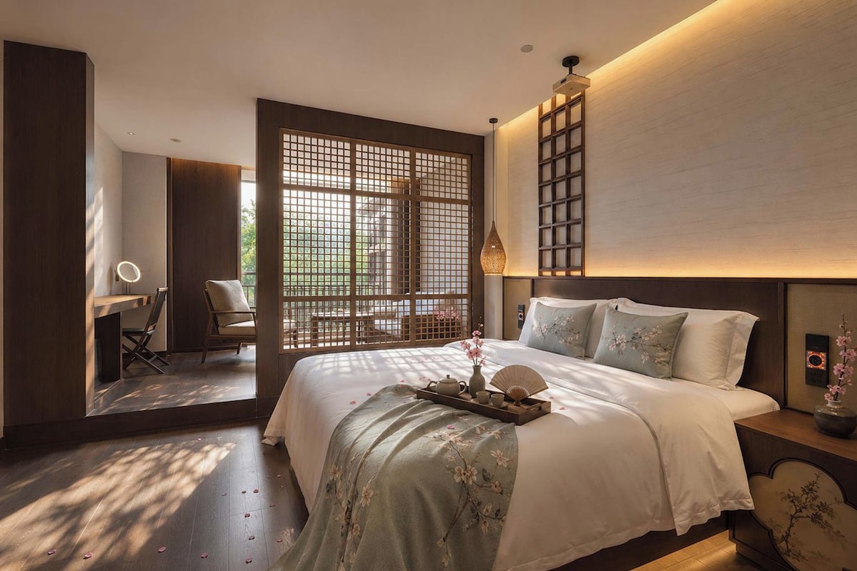 Een moderne slaapkamer met een groot bed, een bureau en uitzicht door een houten scheidingswand.