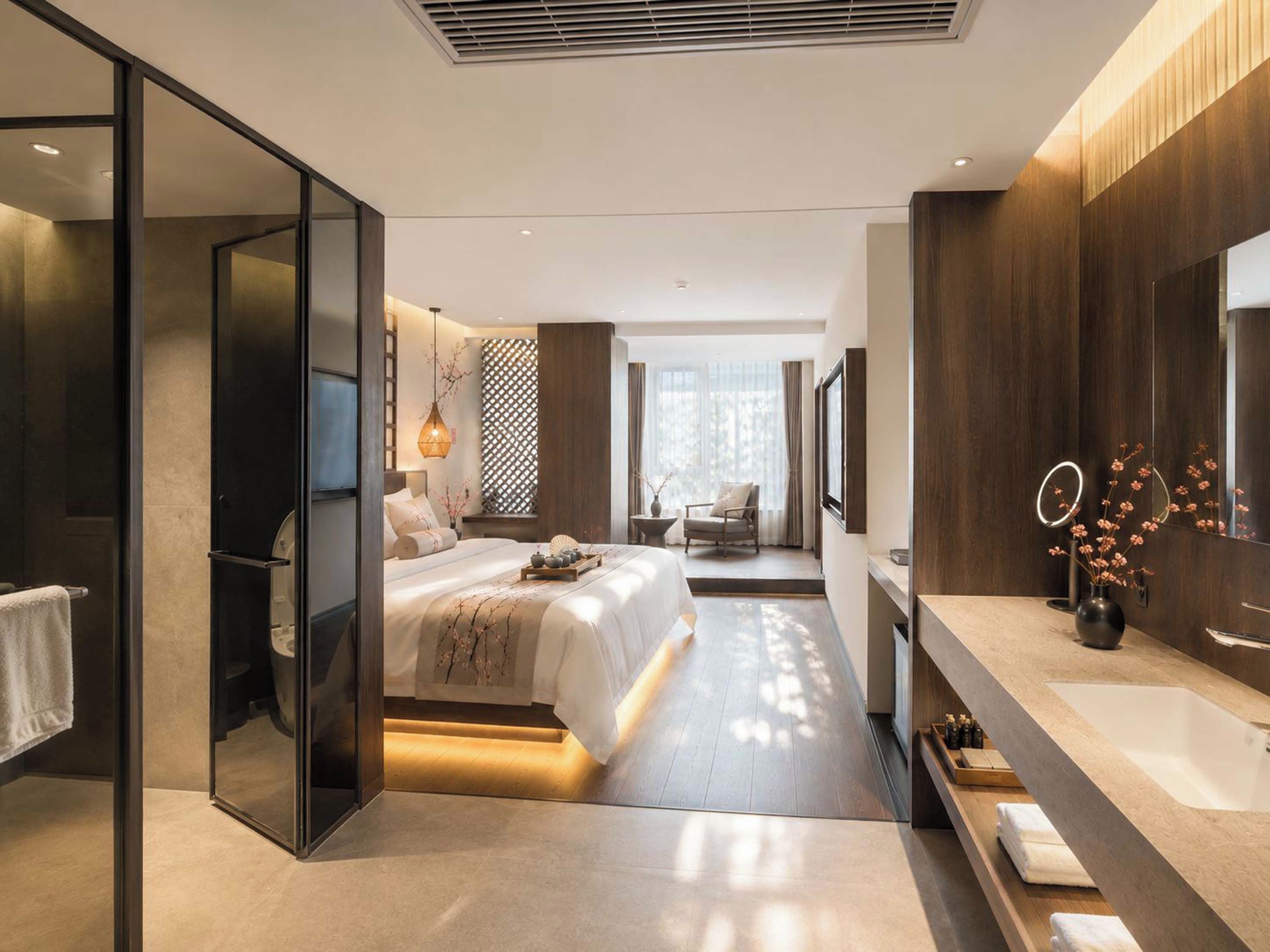 Een moderne slaapkamer met een groot bed, een inloopkast, een kaptafel met spiegel en uitzicht op de natuur.