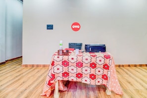 Un salón de conferencias con una mesa cubierta por un mantel floral, una silla azul, una impresora negra y un letrero rojo en la pared.