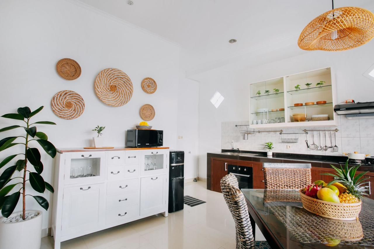 Cocina moderna con armarios blancos, una mesa de comedor de vidrio y una cesta de mimbre con fruta.
