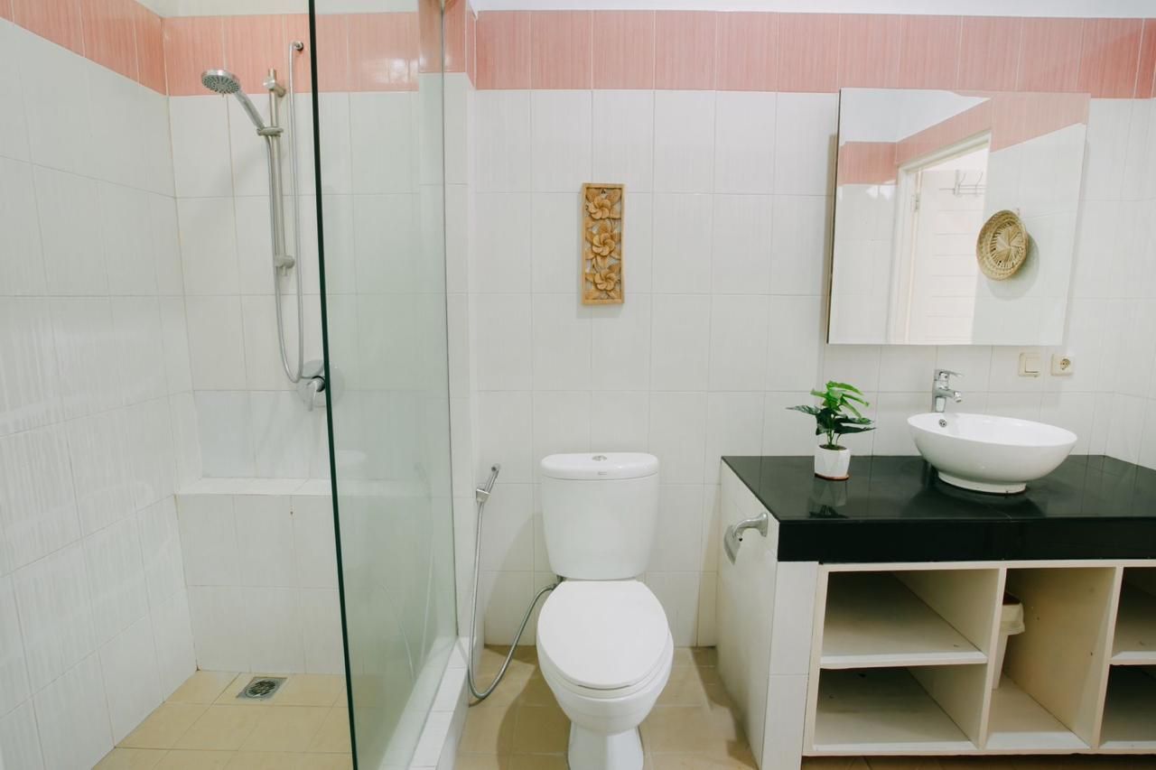 Un baño con ducha envuelta en vidrio, inodoro blanco, encimera negra con lavamanos y un espejo.