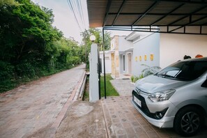 A residential driveway with a parked car, a gated entrance, and a house with a light-colored exterior. - House in the Bush (Badung)