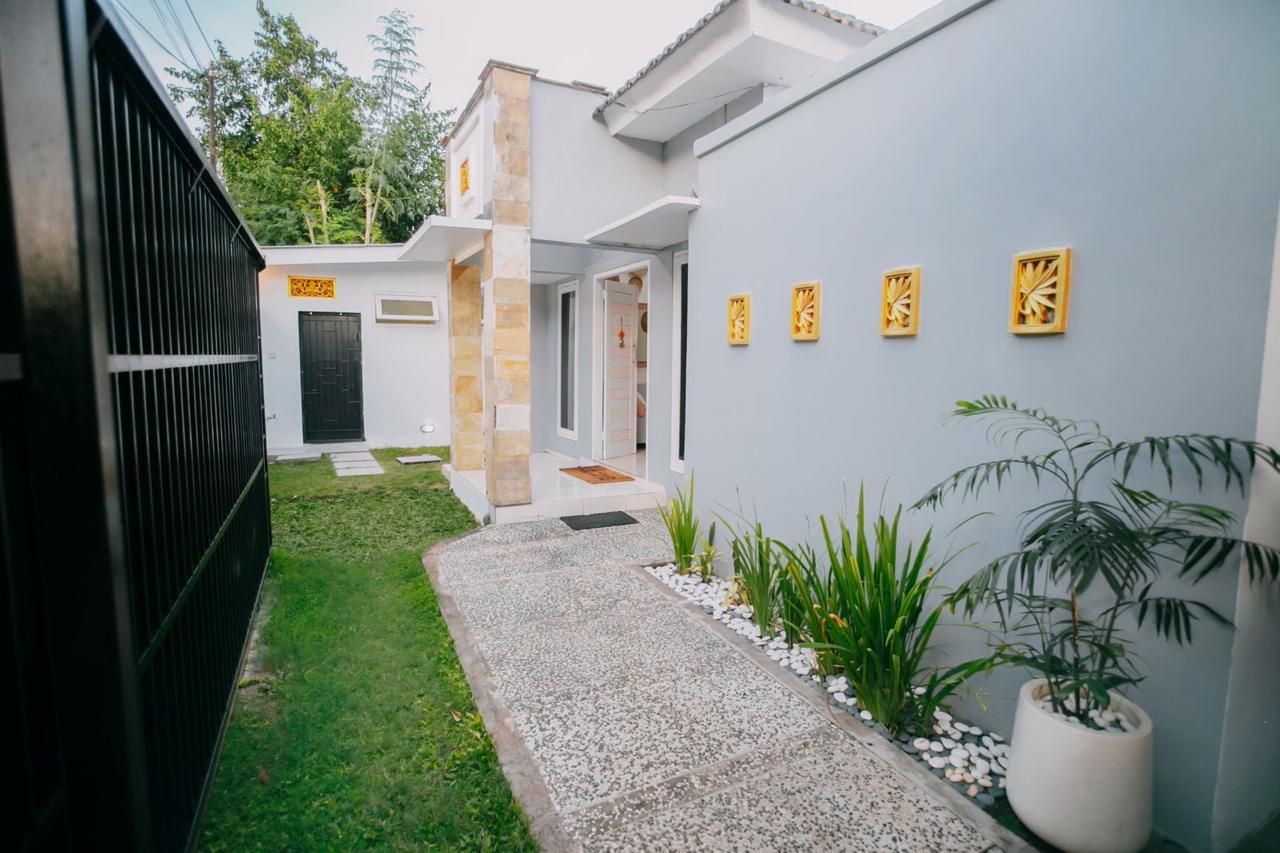 Ein modernes Haus mit gepflastertem Weg, einem schwarzen Zaun und einem kleinen Garten mit Pflanzen und einem Topfbaum.