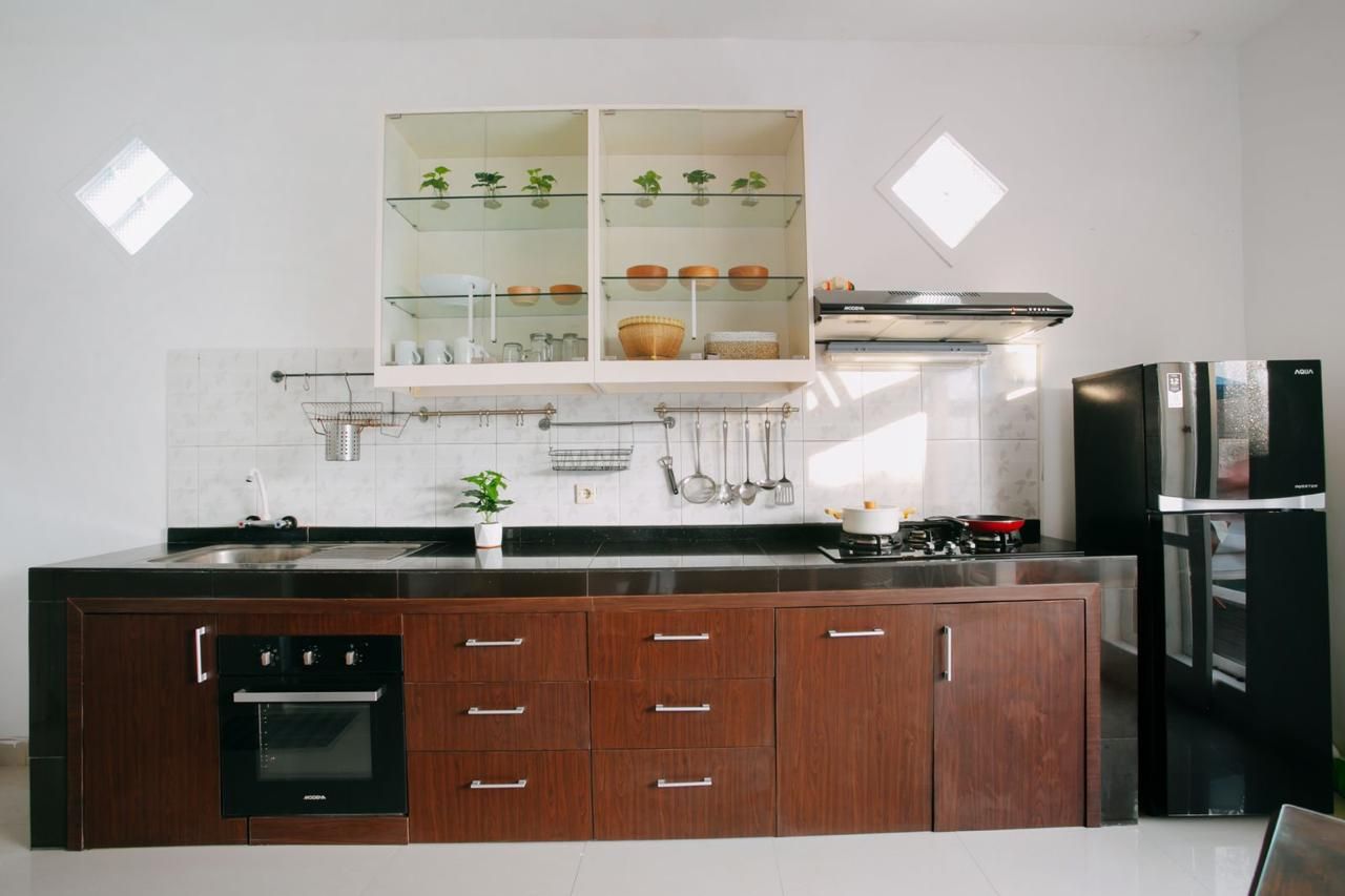 A modern kitchen with a built-in oven, a stainless steel refrigerator, and a glass-fronted cabinet with plants.