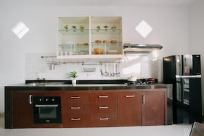 A modern kitchen with a built-in oven, a stainless steel refrigerator, and a glass-fronted cabinet with plants. - House in the Bush (Badung)