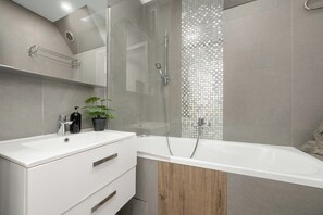 Ein modernes Badezimmer mit einem weißen Waschtisch, einer Duschkabine aus Glas und einem Holzschrank.