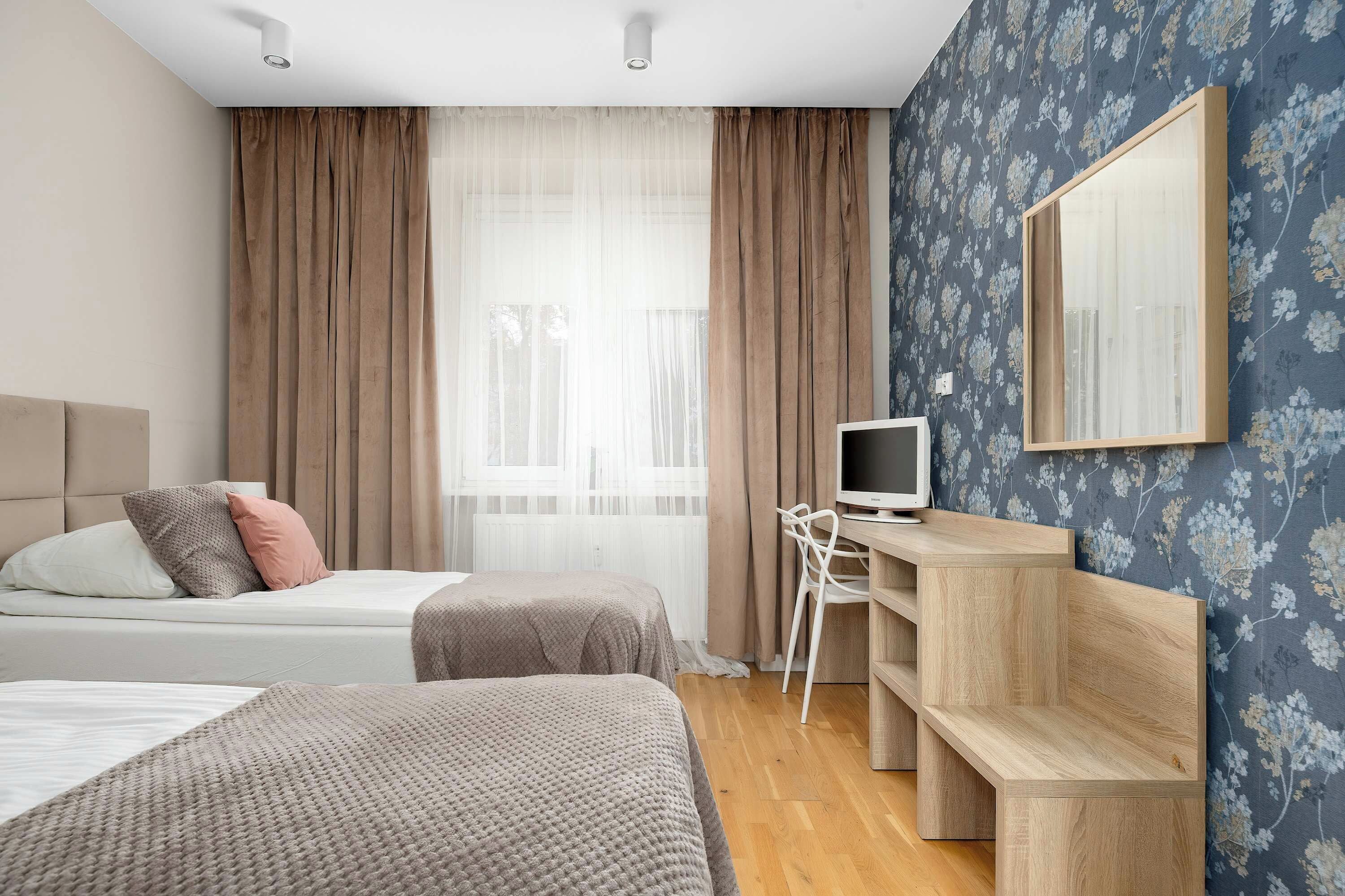 A hotel room with two beds, a desk with a computer, a mirror, and a window with curtains.