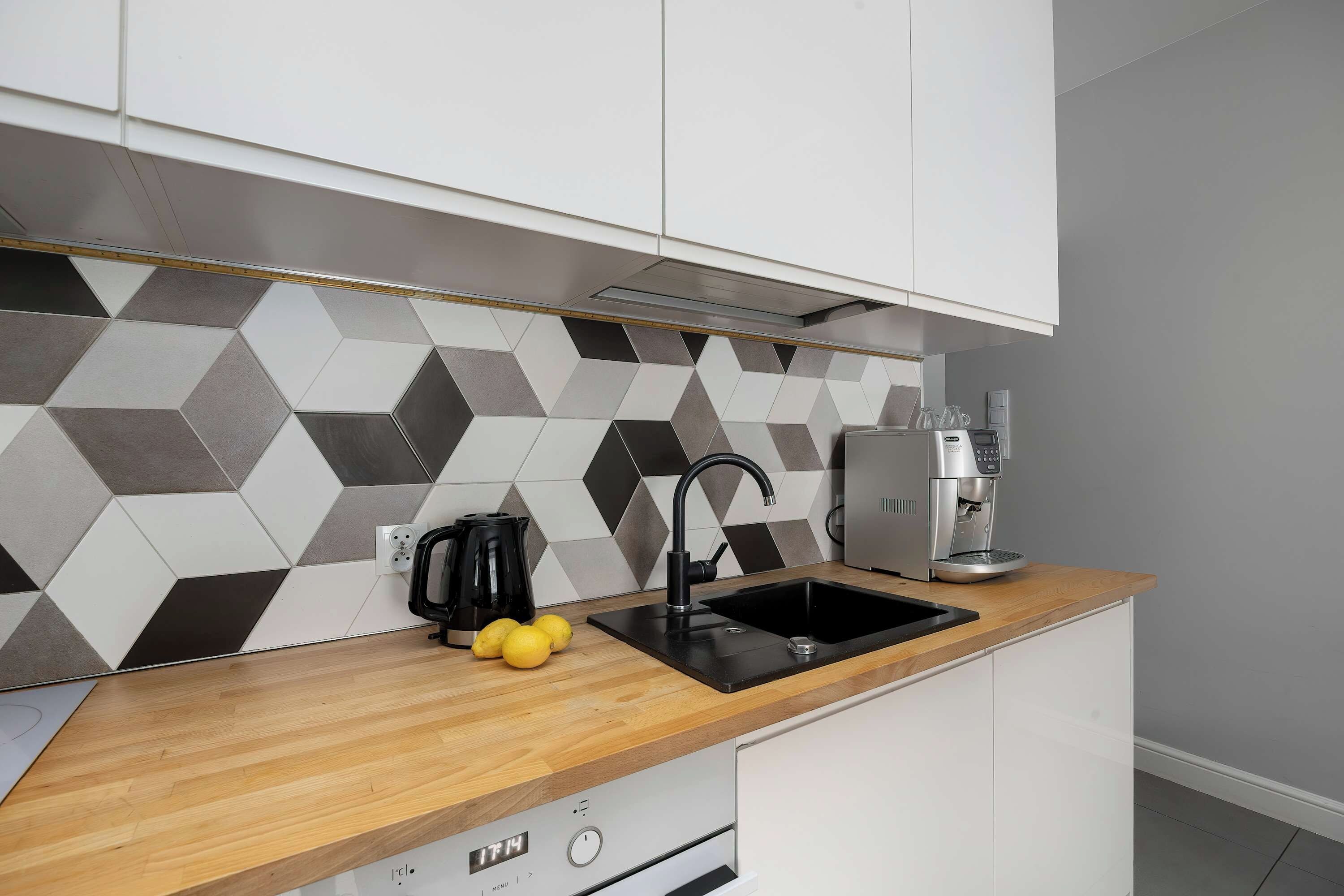 Een moderne keuken met een zwarte spoelbak, een koffieapparaat en een achterwand van honingraatmozaïek.