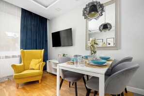 Ein modernes Wohnzimmer mit einem gelben Sessel, einem Esstisch mit blauen Schüsseln und Gläsern, einem Flachbildfernseher und einem großen Spiegel mit Dekorationselementen.