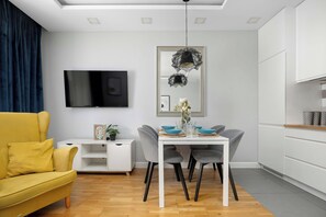 Una sala de estar moderna con un sofá amarillo, una mesa de comedor con sillas, un televisor de pantalla plana montado en la pared y un espejo decorativo sobre la mesa.