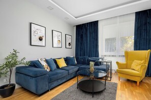 Una sala de estar moderna con un sofá azul, un sillón amarillo y una mesa de centro. Hay cuadros enmarcados en la pared y una planta en maceta.