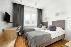 Ein modernes Hotelzimmer mit zwei Betten, einem Schreibtisch, einem Sessel und einem Fernseher.