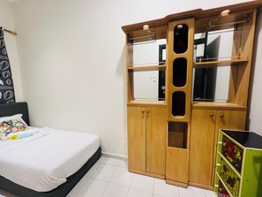 Quarto com cama, guarda-roupa de madeira com vários compartimentos e um armário verde com desenhos florais.