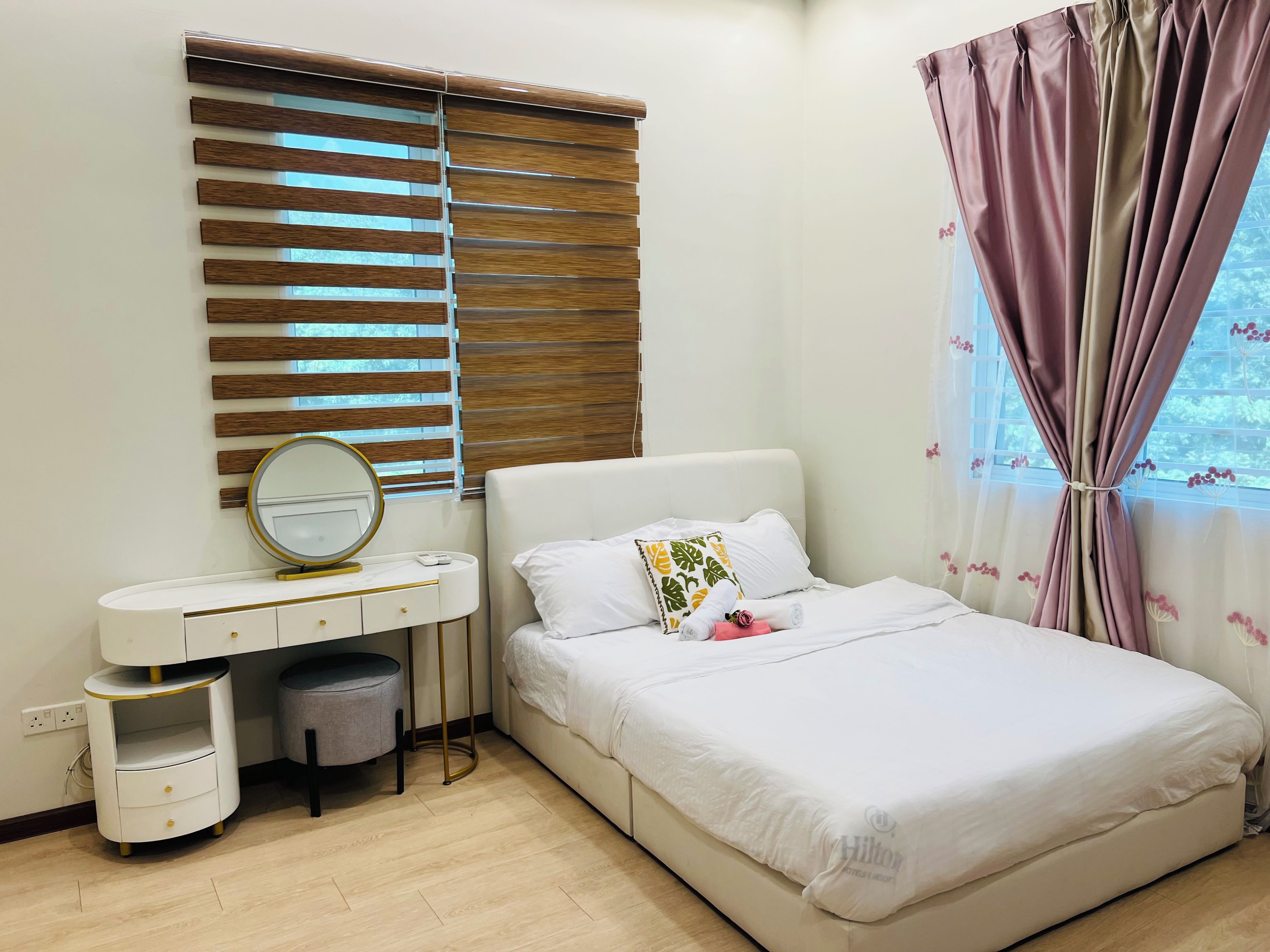 A bedroom with a bed, a bedside table with a mirror, a small storage unit, and a window with curtains.