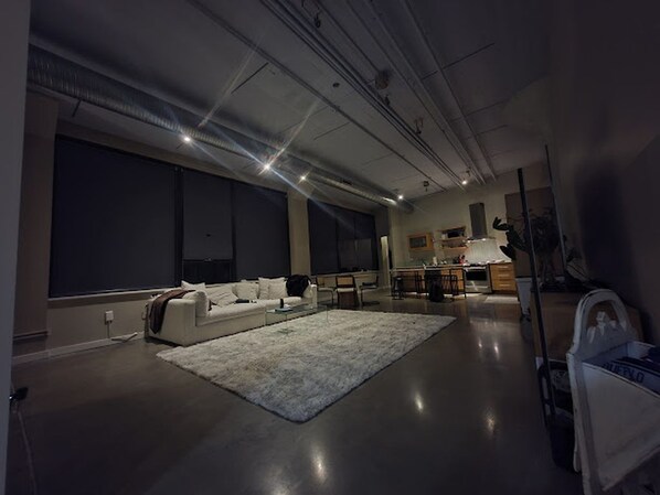 A modern living room with a large window, a white sofa, a coffee table, and a kitchen area in the background. - Waterfront location for rent with great quick escape! (North Tonawanda)