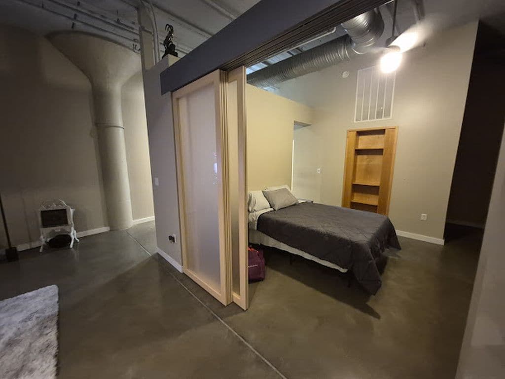 Ein Schlafzimmer mit einem Bett, einem Holzschrank, einem Haustierbett und einem kleinen Tisch.