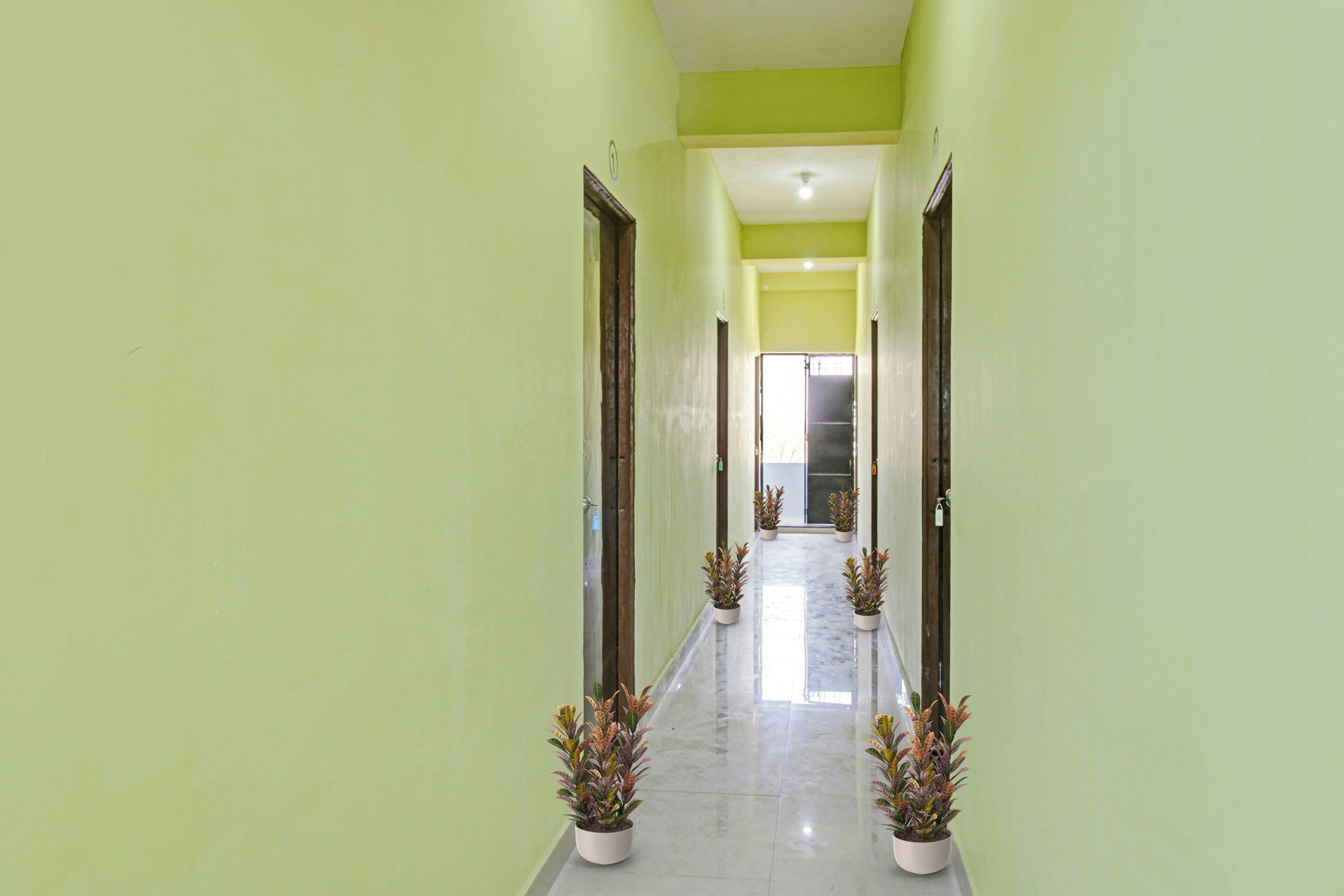 A corridor with green walls and doors, leading to a bright room with a large window.