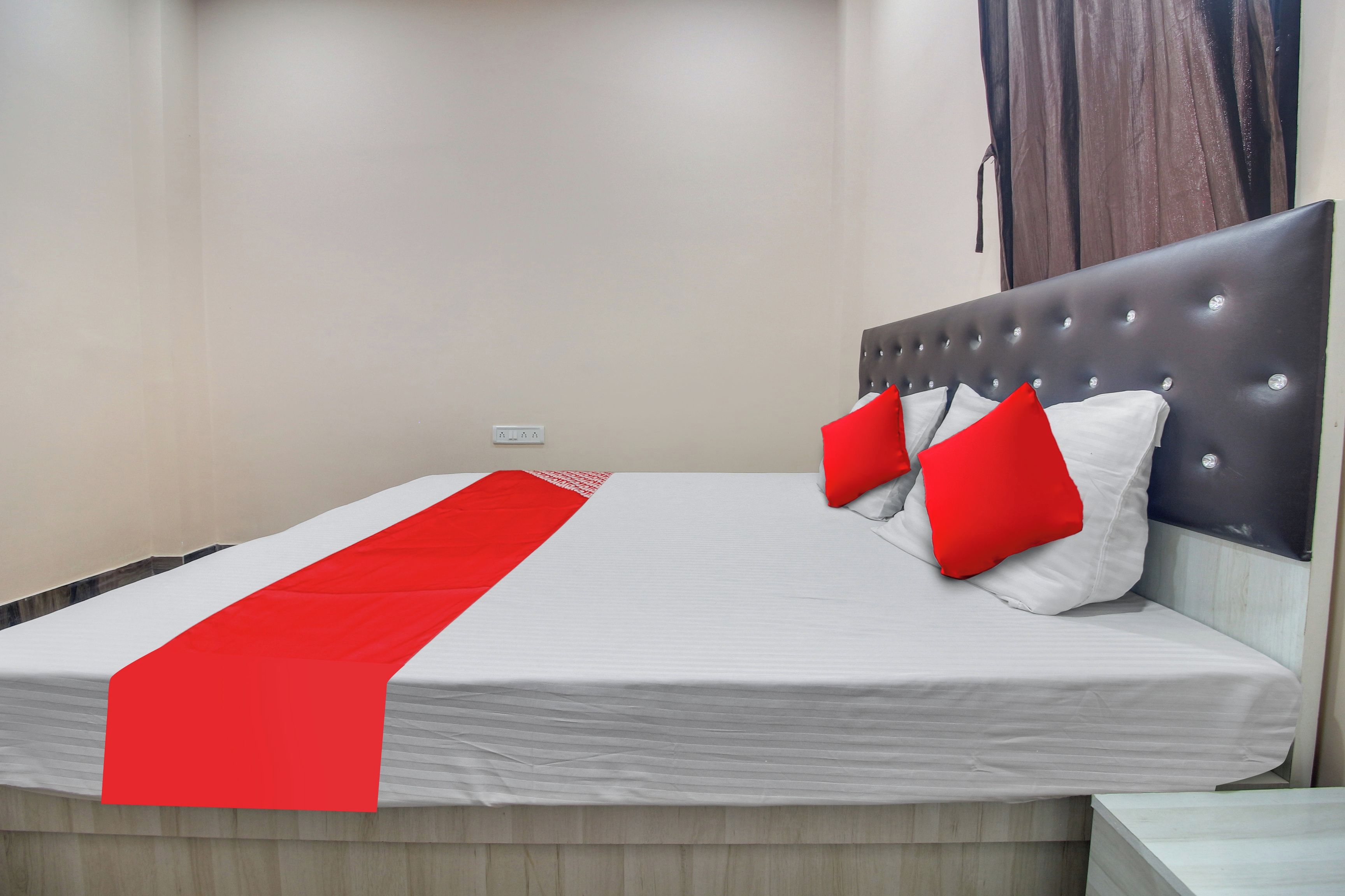A neatly made bed with a white and red bedspread, two red pillows, and a grey upholstered headboard.
