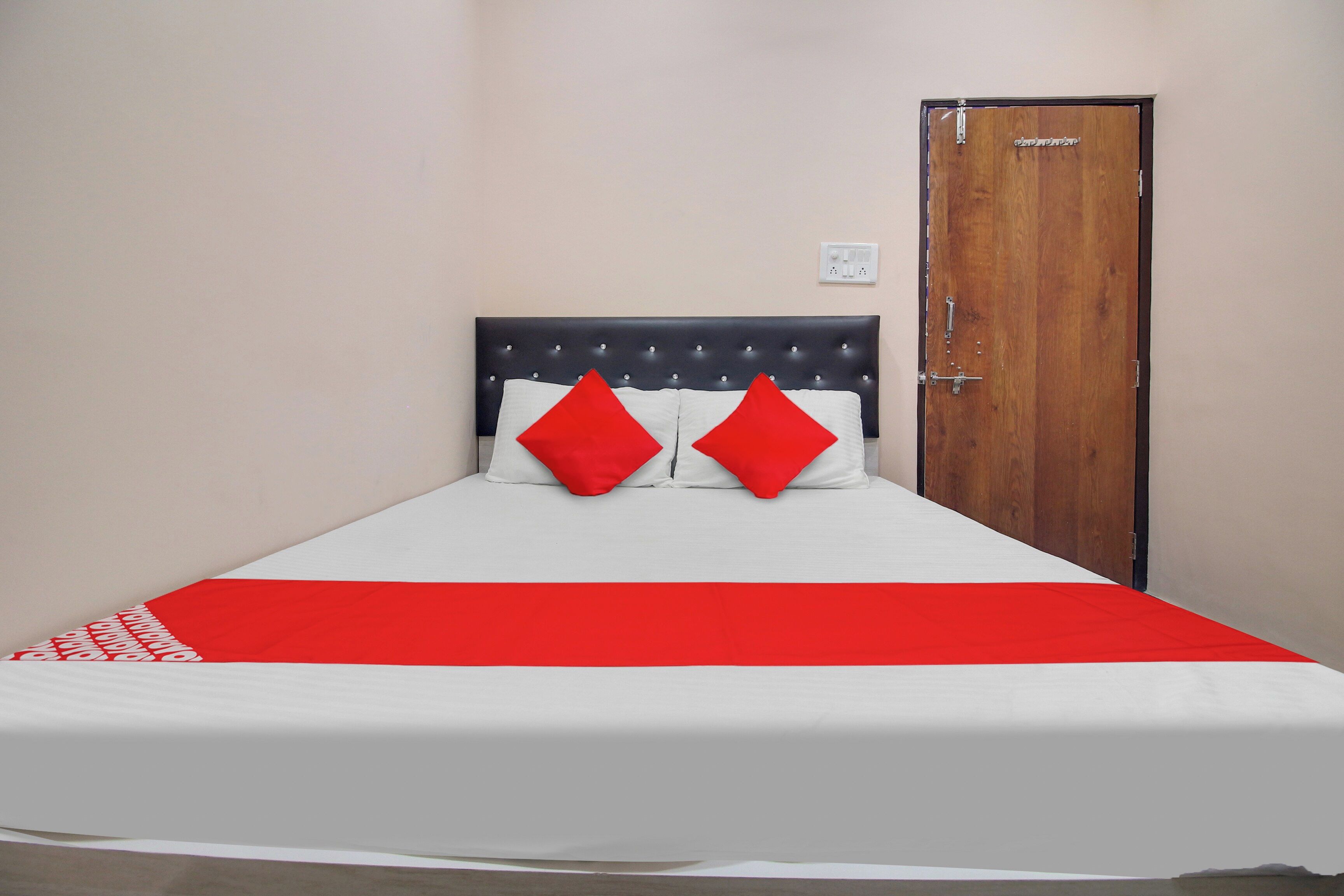 Una cama con una colcha blanca y roja, dos almohadas rojas y un cabecero negro.