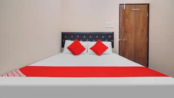 Una cama con una colcha blanca y roja, dos almohadas rojas y un cabecero negro.
