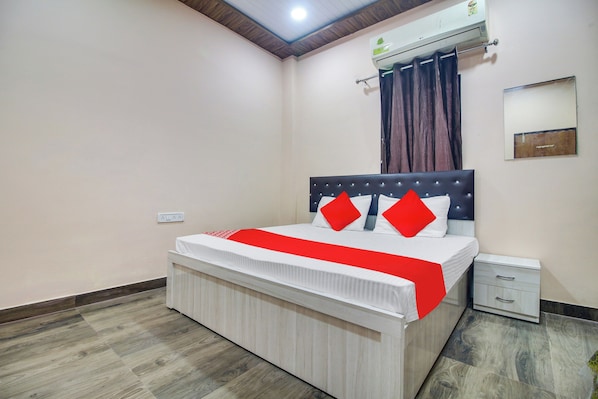 Un dormitorio con cama, mesita de noche, aire acondicionado de pared y ventana con cortinas.