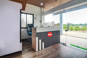 Un área de recepción de oficina con un escritorio de madera, una silla de oficina negra, una computadora portátil y una puerta de vidrio que da al exterior.