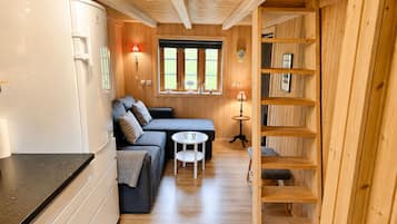 Een compact interieur met houten lambrisering, een kitchenette, een bank, een kleine ronde tafel en een inbouwkast.
