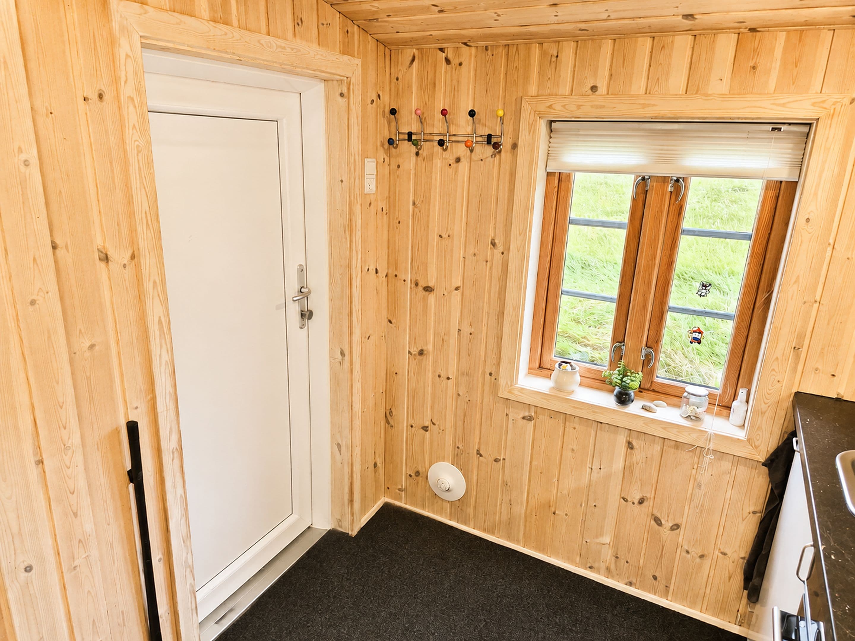 Een kamer met houten lambrisering, een witte deur en een raam met uitzicht op groen, plus een klein plankje met spullen.