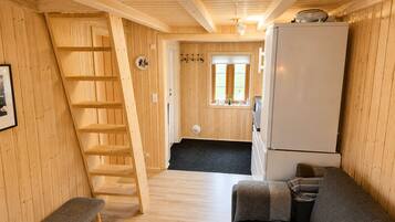 Een houten interieur met een bank, een koelkast, een ladder en een deur naar een badkamer.
