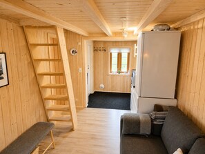 Un intérieur en bois comprenant un canapé, un réfrigérateur, une échelle et une porte donnant accès à une salle de bain.