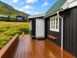 Une terrasse en bois avec un banc, une porte et une fenêtre, sur un bâtiment à l’extérieur sombre.